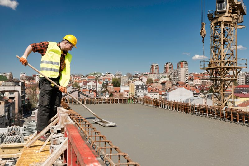 builder smoothing concrete surface on top of a tall building