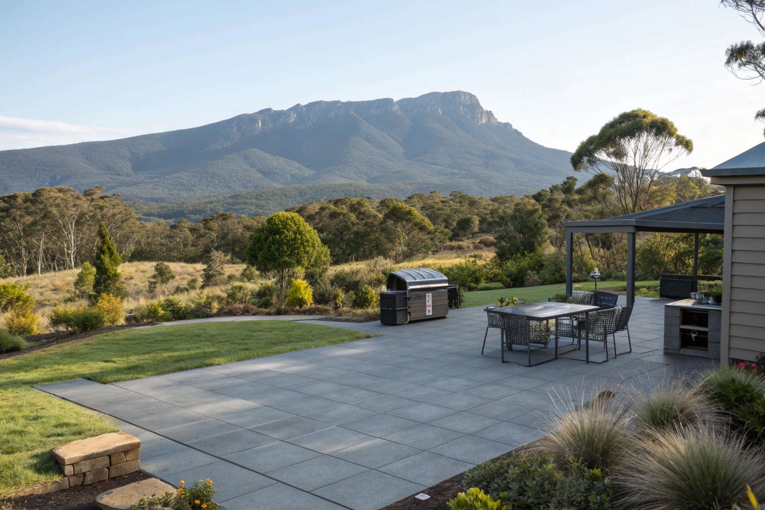 A charcoal grey coloured concrete patio area with outdoor furniture and barbecue setup